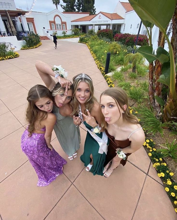 four young women posing for a photo in front of a flowered garden and walkway