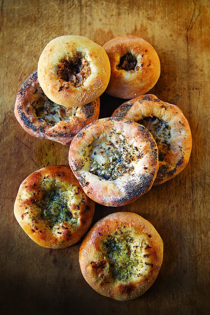 four bagels with pesto on them sitting on top of a wooden table next to each other