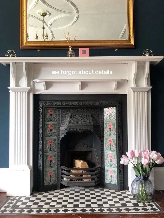 a fireplace with a mirror above it and flowers in vases on the floor next to it