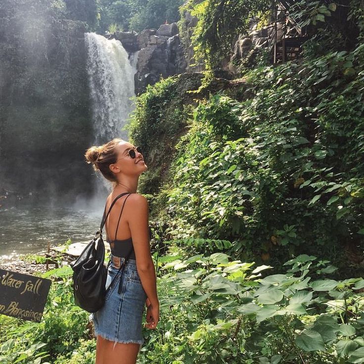 a woman standing in front of a waterfall looking up at the sky with her eyes closed