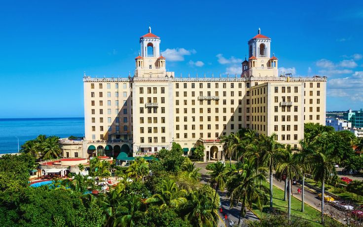 a large white building with two towers and palm trees in the foreground, on a sunny day