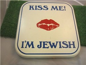 a sign that says kiss me i'm jewish on the ground next to grass