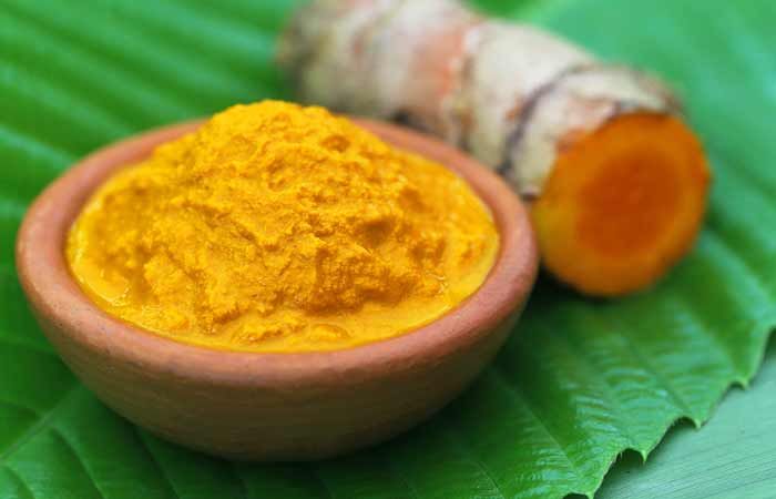 tumerical powder in a bowl next to a ginger root on a green leaf