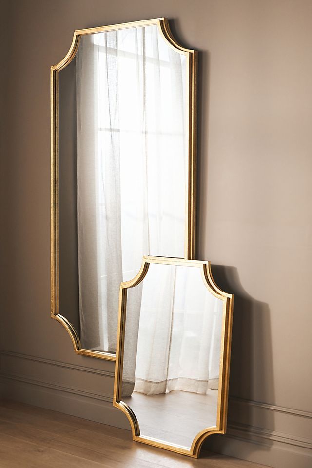 a mirror sitting on top of a wooden floor next to a white curtained window