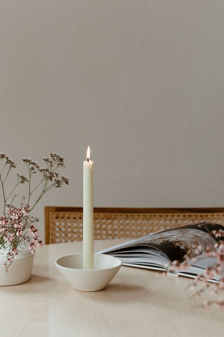 a white candle sitting on top of a wooden table next to a bowl filled with flowers