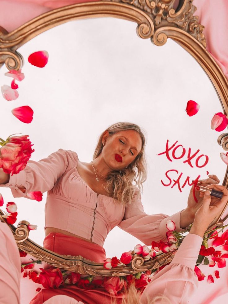 a woman in a pink dress looking at herself in a mirror with roses on it