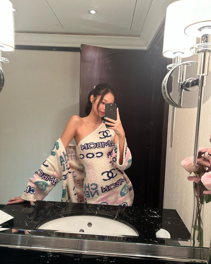 a woman taking a selfie in front of a bathroom mirror with flowers on the counter