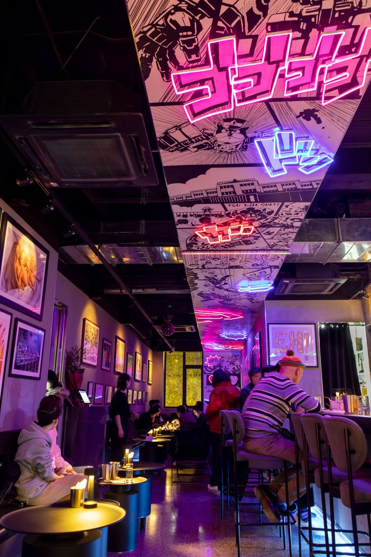 people are sitting at tables in a brightly lit room with neon signs on the ceiling