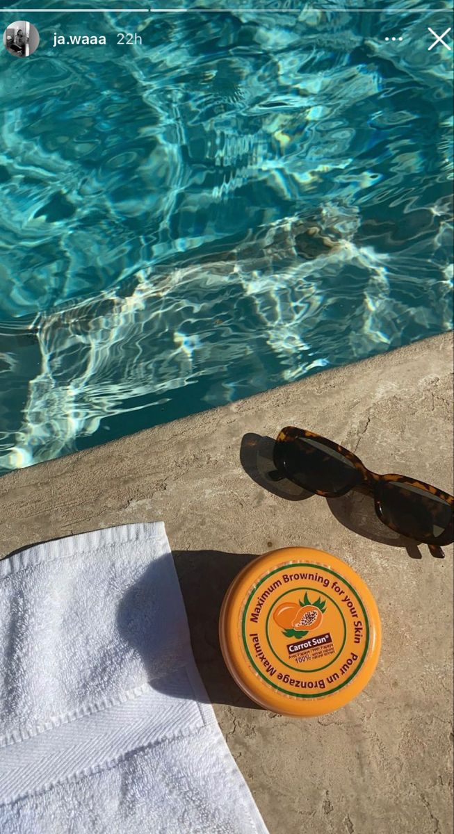 an orange frisbee and sunglasses sitting on the edge of a swimming pool next to a towel