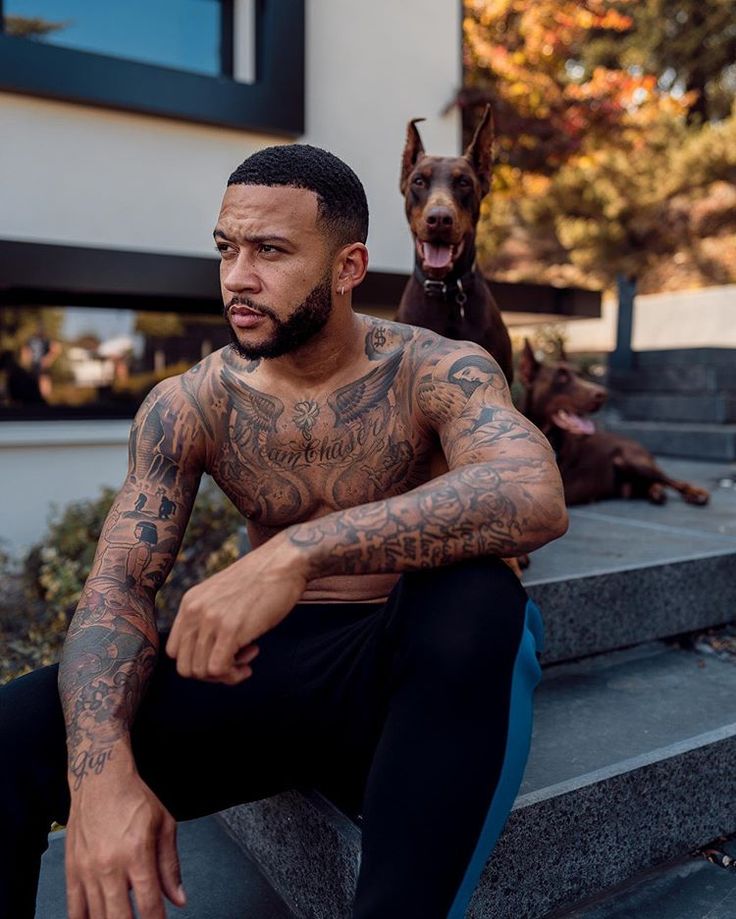 a man with tattoos sitting on steps next to a dog and looking at the camera