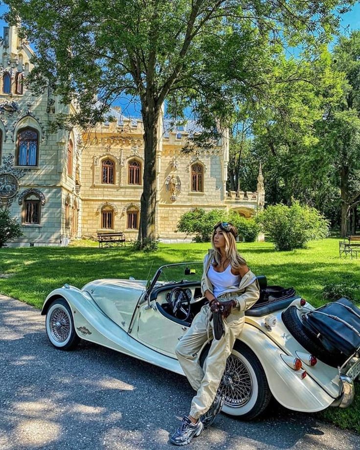 a woman sitting on top of a white sports car in front of a large building