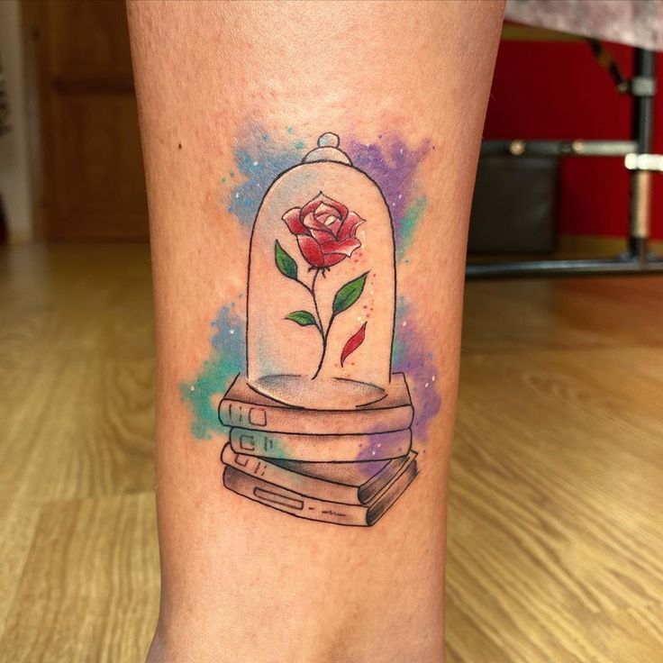 a tattoo on the leg of a woman with a rose in a glass dome and books