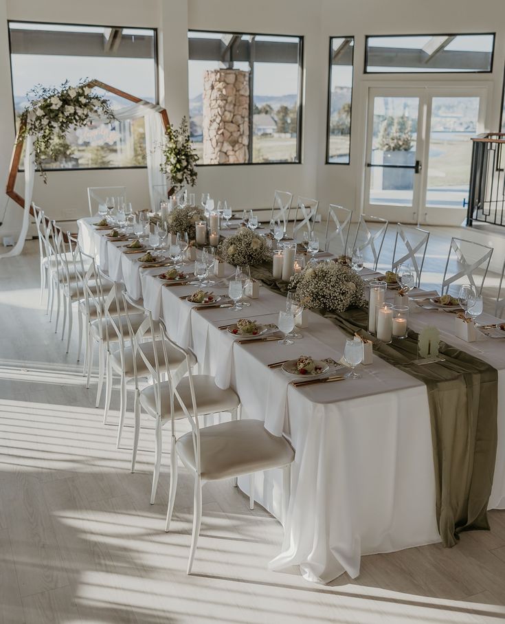 a long table is set with white linens and greenery for an elegant wedding reception