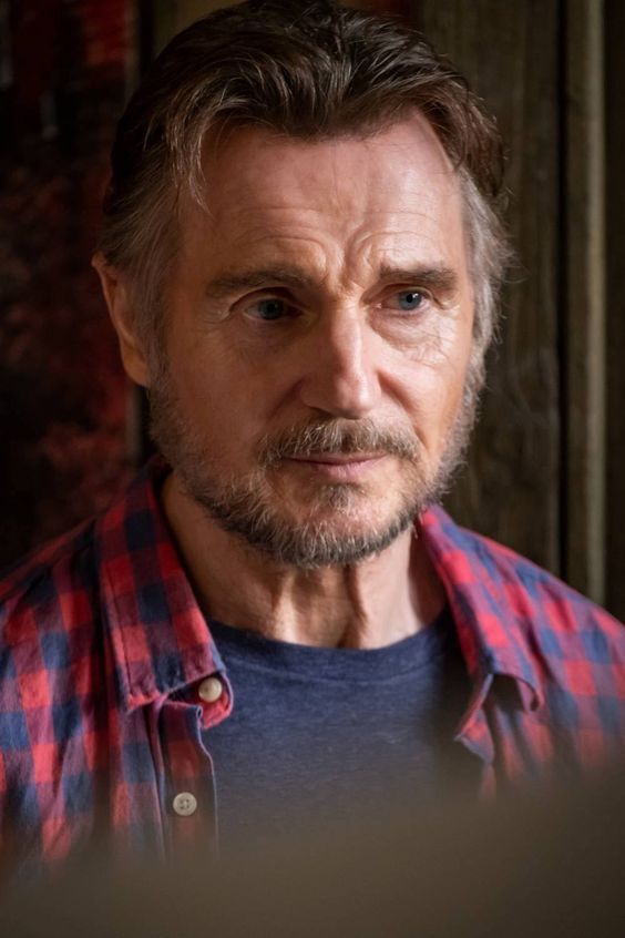 an older man with grey hair wearing a red and blue checkered shirt looking at the camera