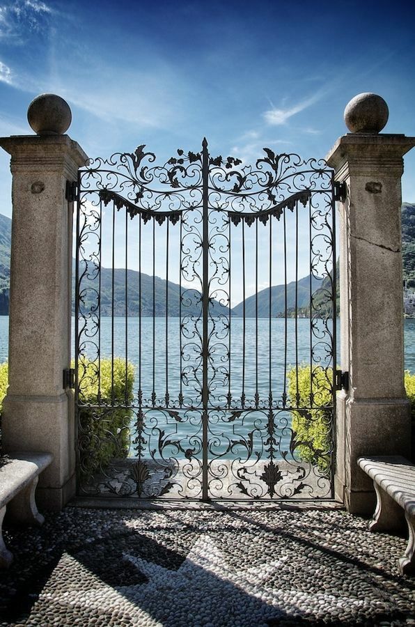 an iron gate with two benches in front of it and the water behind it on a sunny day