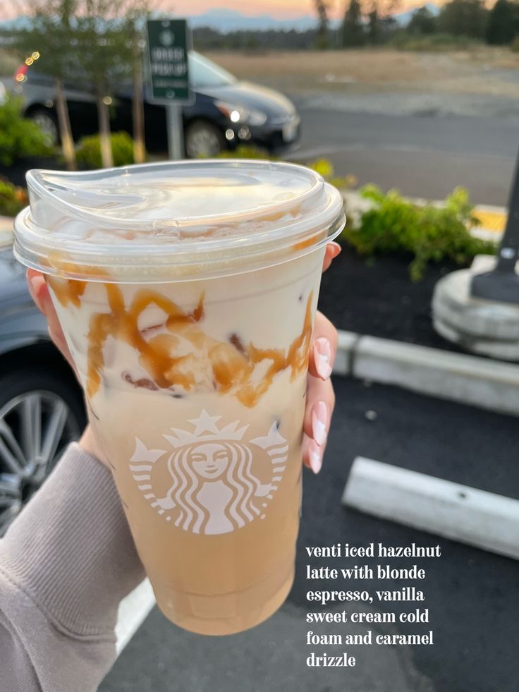 a person holding up a starbucks drink in front of a parking lot