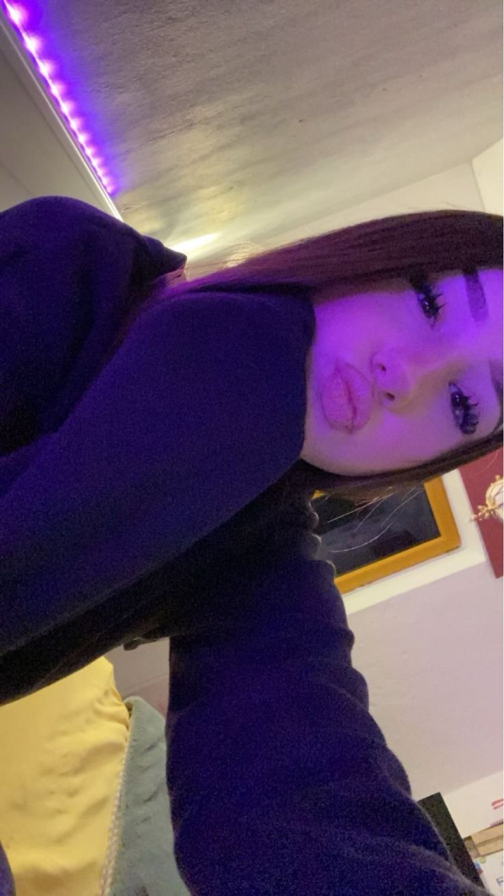 a woman with dark hair is taking a selfie in front of the camera, wearing a purple hoodie