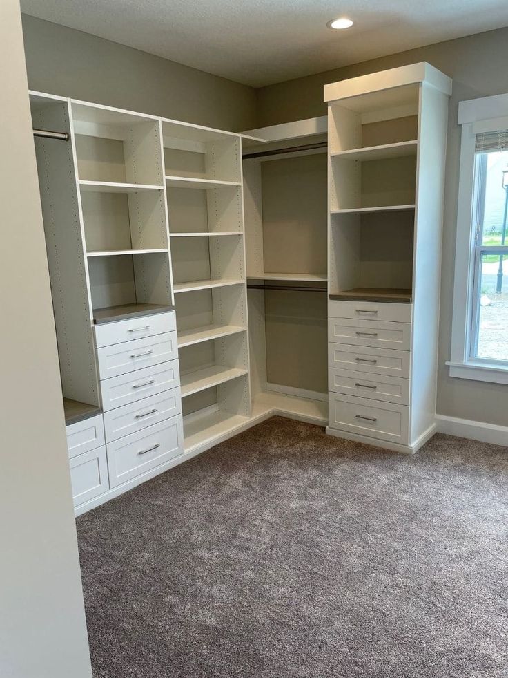 an empty walk in closet with white drawers and gray carpeted flooring is shown