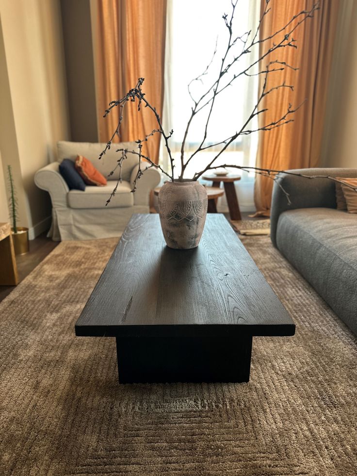 a vase sitting on top of a wooden table in front of a couch and window