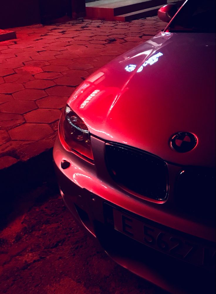 a red car is parked on the side of the road at night with its lights on