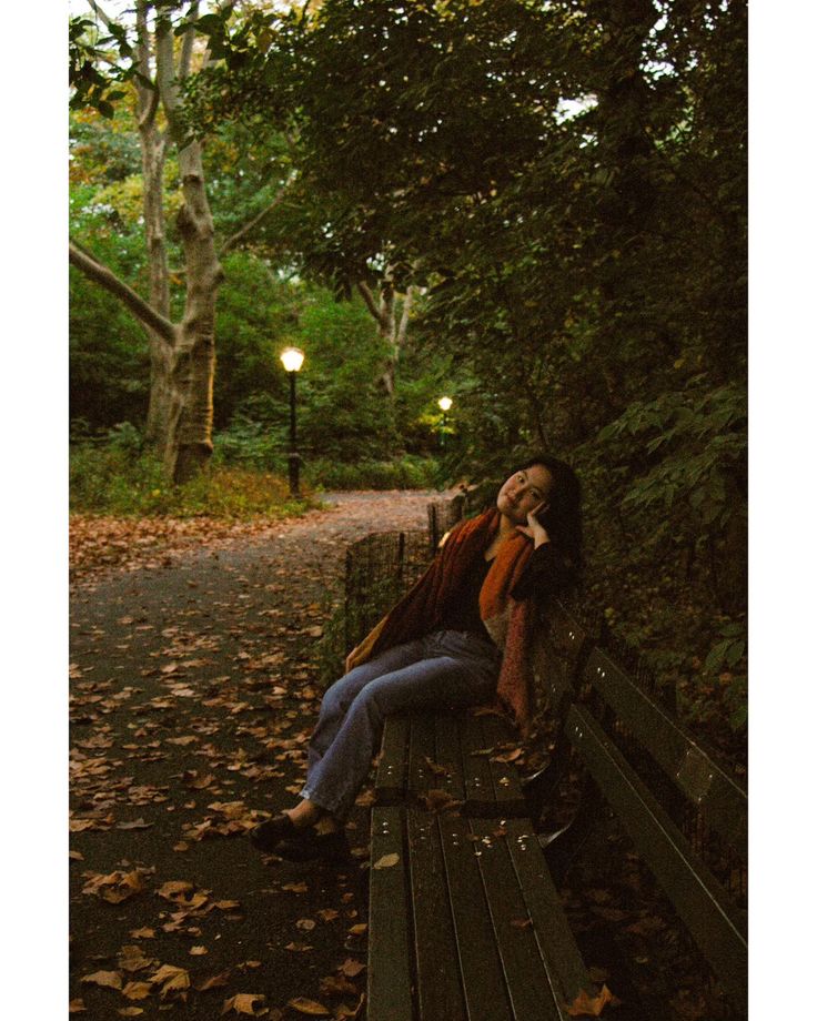 a woman is sitting on a park bench talking on her cell phone while the sun sets