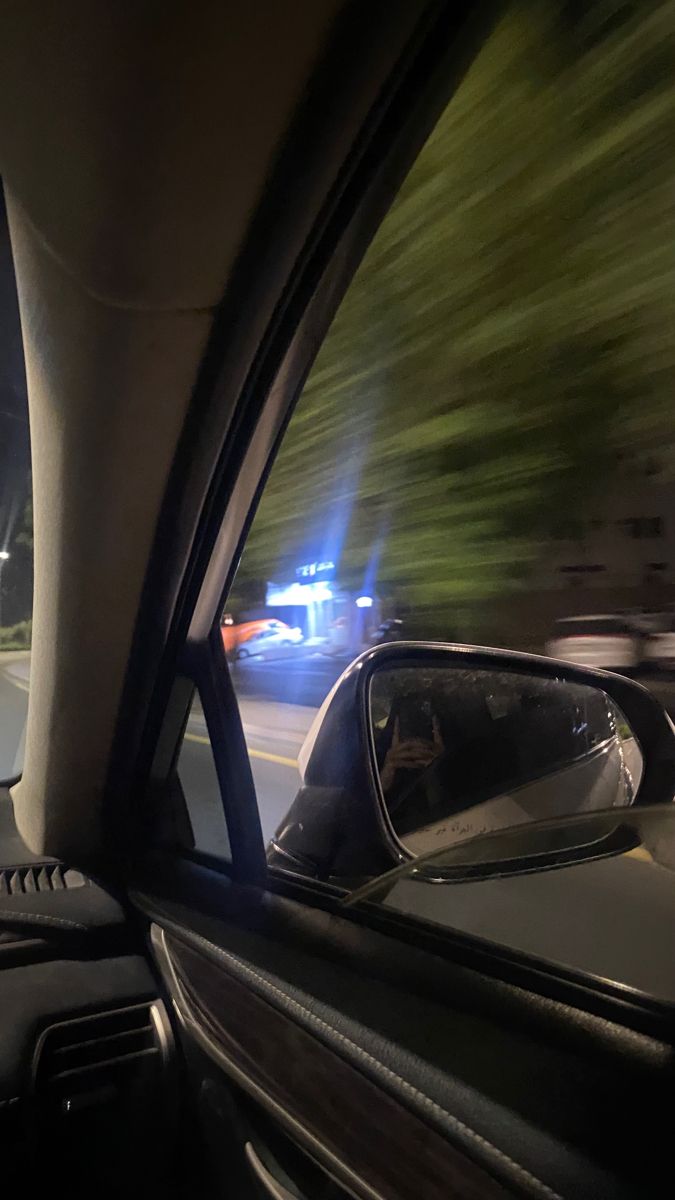 a car driving down the road at night with its lights on and it's rear view mirror showing