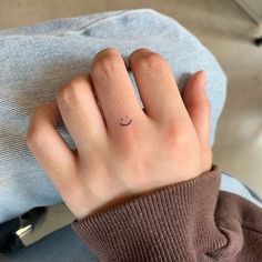 a woman's hand with a small smiley face tattoo on her left ring finger