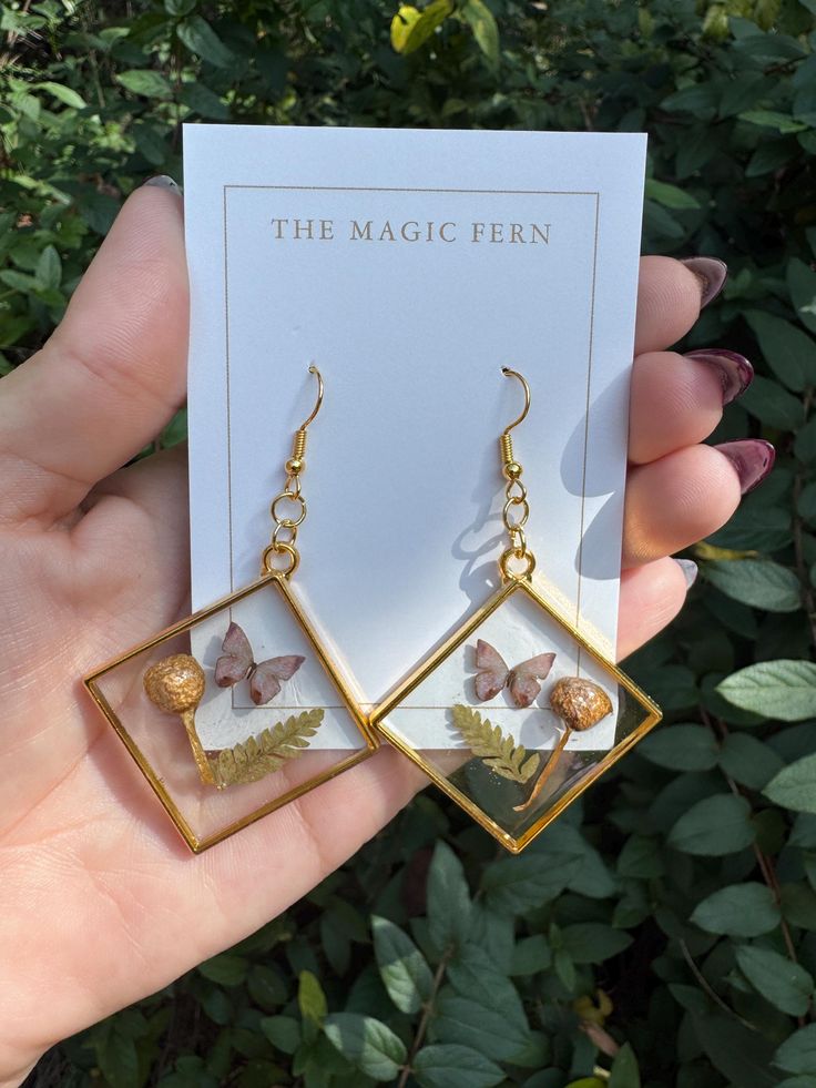 the magic fern earrings are shown in front of a green bush with leaves on it