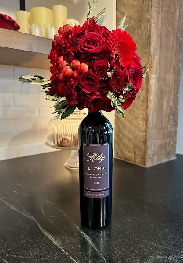 a vase filled with red flowers sitting on top of a counter next to a bottle of wine