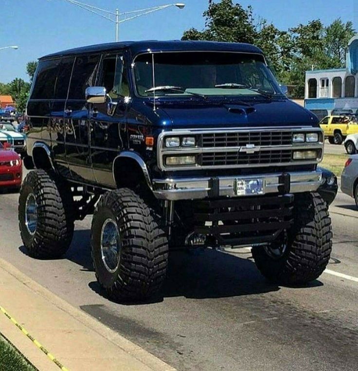 a large black truck driving down a street next to parked cars on the side of the road