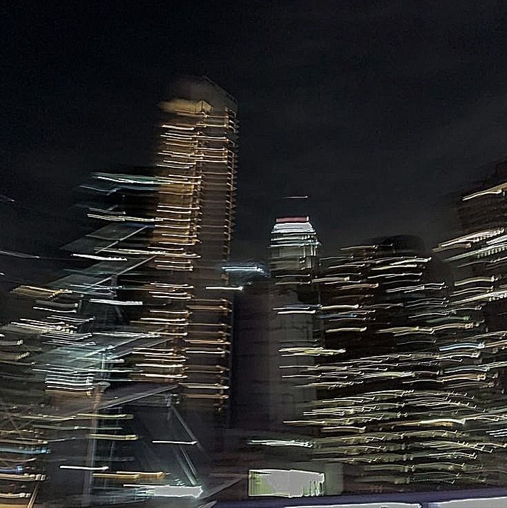 blurry photograph of city skyline at night with skyscrapers in the foreground and bus on roadway