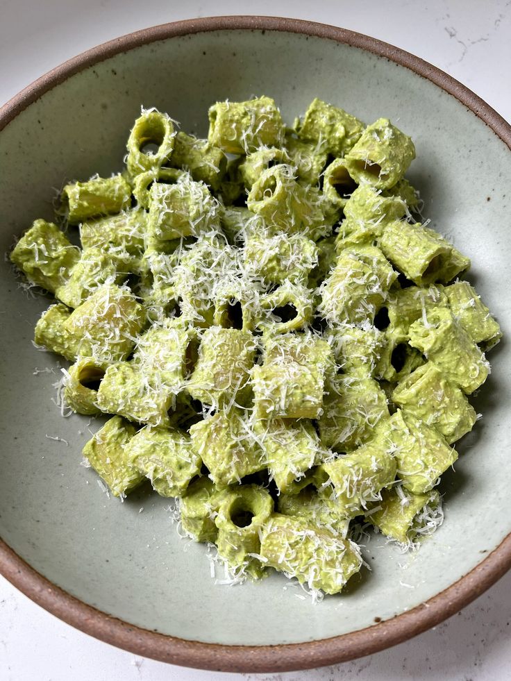 a white bowl filled with green pasta covered in parmesan cheese