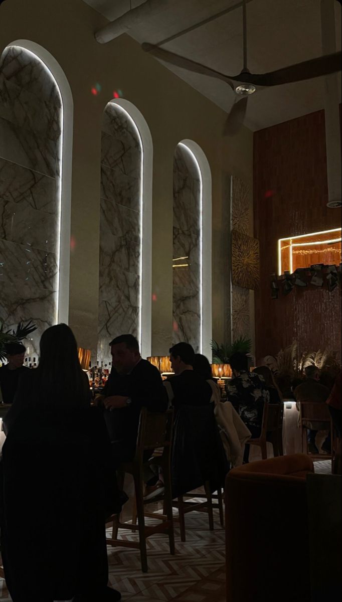 people are sitting at tables in a dimly lit room with tall columns and floor to ceiling windows