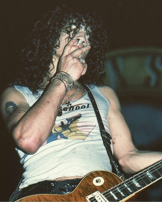 a man with curly hair holding a guitar in his hand and singing into the microphone