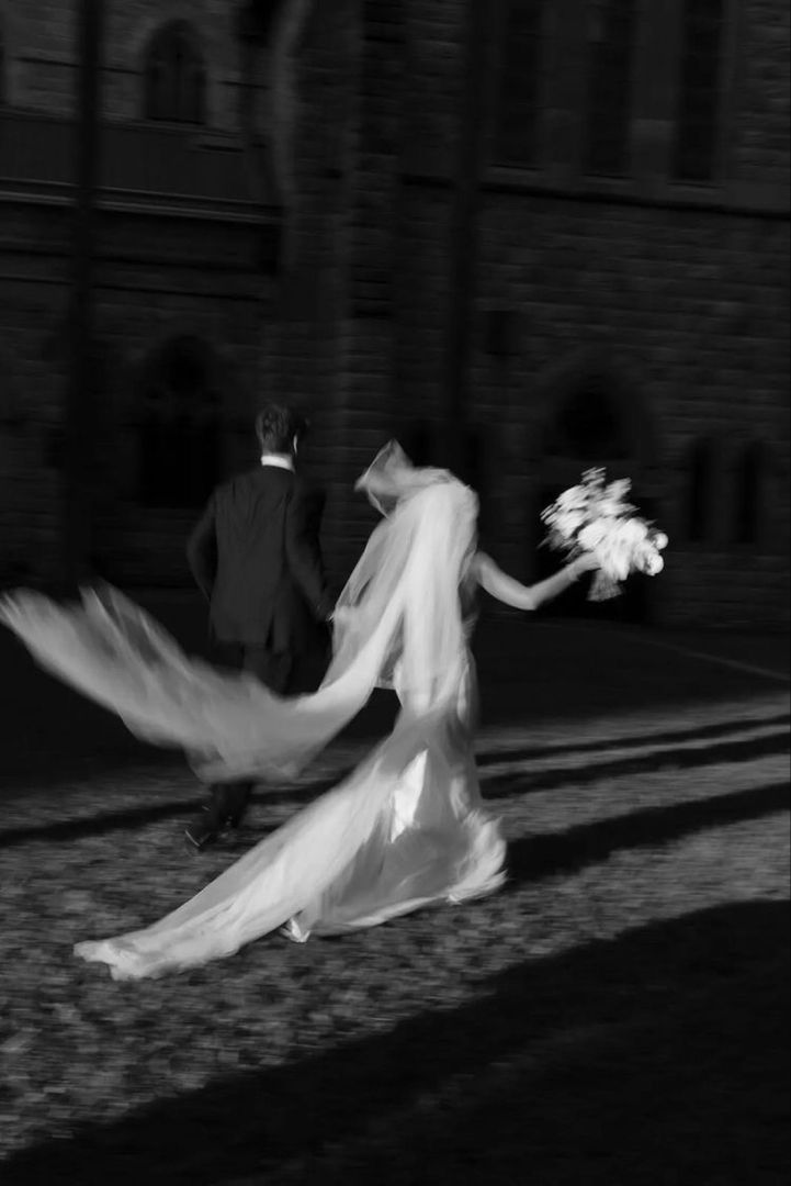 the bride and groom are walking down the street with their veils flying in the wind