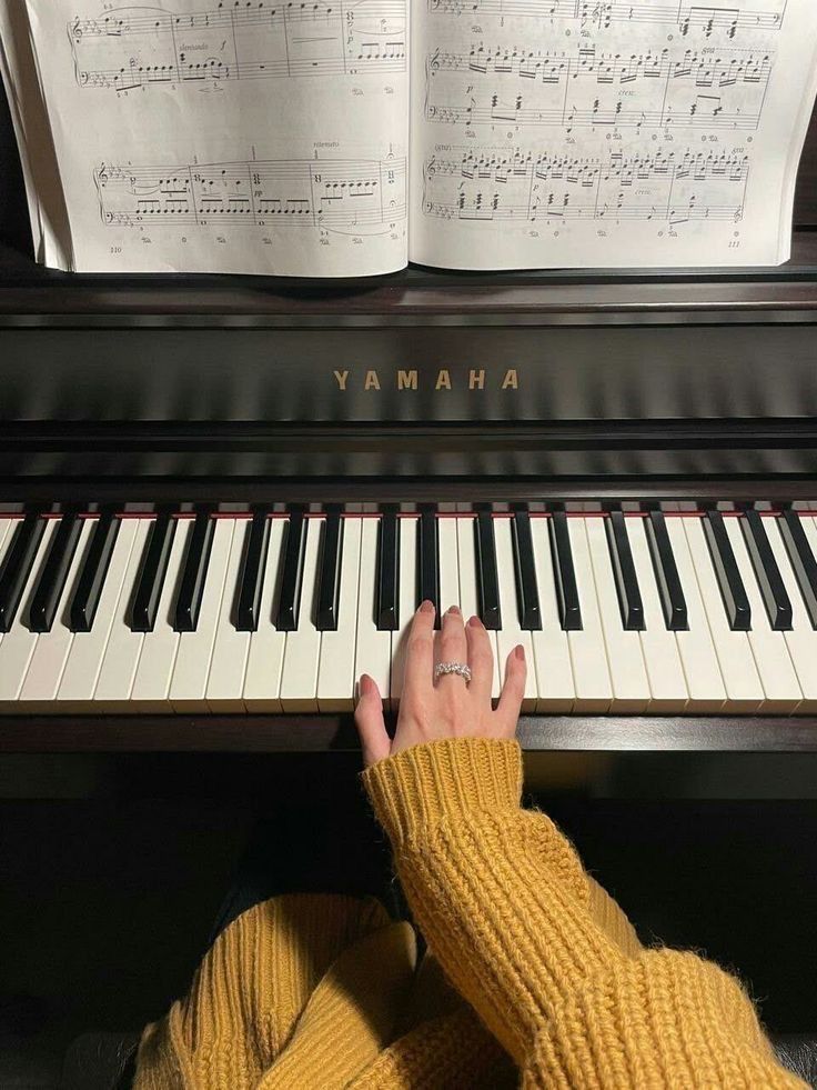 a person sitting at a piano with their hands on the keyboard and sheet music behind them