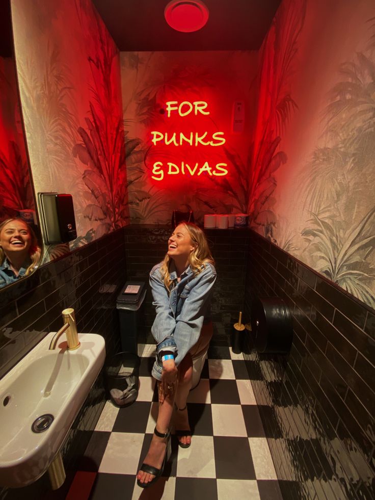 two women sitting in a bathroom with red lights on the wall and black and white checkered floor