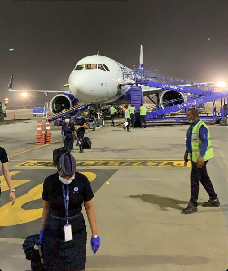 several people walking towards an airplane on the tarmac at night with other workers nearby