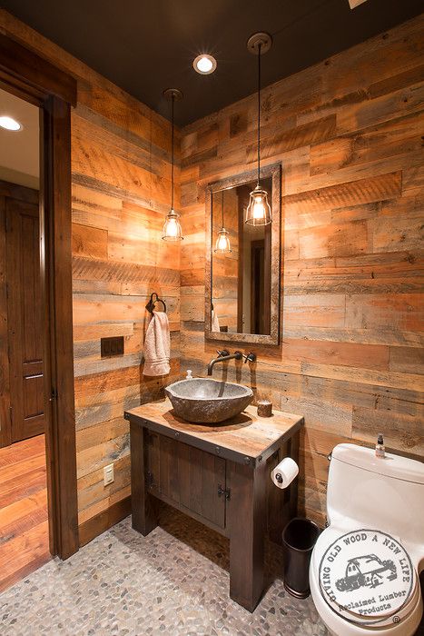 a bathroom with wooden walls and flooring has a toilet, sink, and mirror