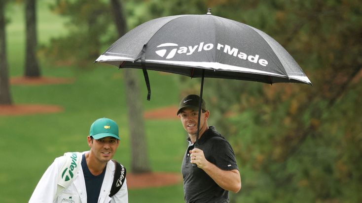 two men standing under an umbrella on a golf course, one holding the other's hand