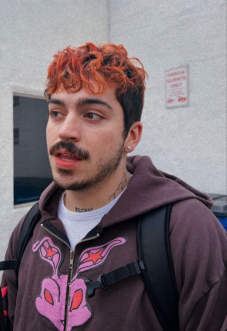 a man with red hair and a moustache on his face wearing a backpack