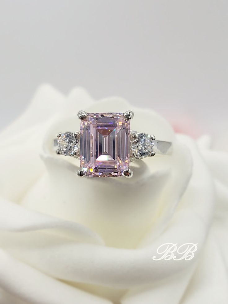 "This Bohn Beauty features a light pink, 5A quality emerald cut cubic zirconia stone in a 925 unplated sterling three stone ring with trellis interweaving prongs. Made to order. Please allow 3 weeks for the production of your ring. Center Stone Weight: 2.5 Carats Diamond Equivalent Approximately Gem Type: Lab Created Cubic Zirconia Shape: Emerald Cut Size: 9x7MM Color: Light Pink Quality: 5A Hardness: 8.5 Mohs Accent Stones Weight: 0.3 Carats Diamond Equivalent Approximately Gem Type: Lab Create Light Pink Ring, Pink Emerald Cut Engagement Ring, Pink Stone Engagement Rings, Famous Engagement Rings, Pink Diamond Earrings, Pink Diamond Engagement Ring, Pink Wedding Rings, Pink Emerald, Pink Diamond Ring