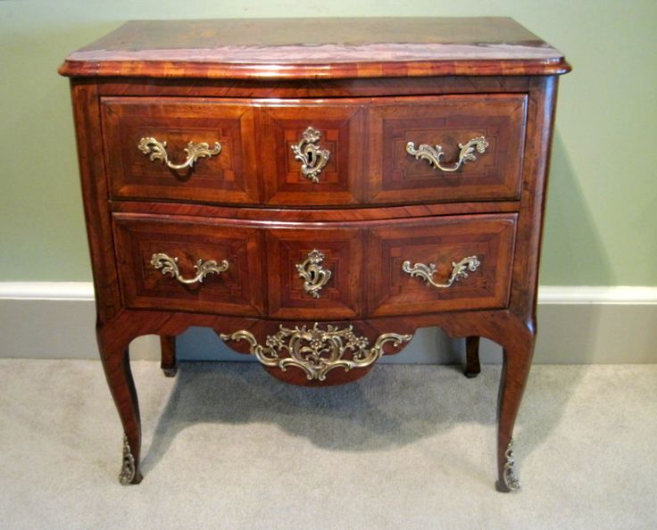 an antique chest of drawers with brass hardware on the top and bottom, sitting against a wall