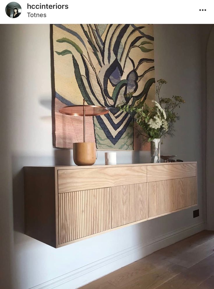 a painting hanging on the wall next to a wooden cabinet with vases and flowers