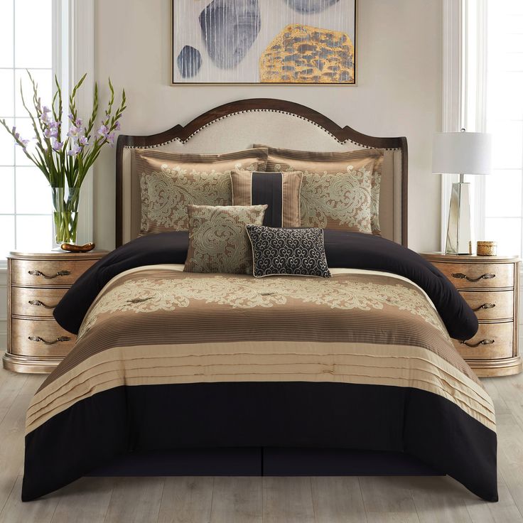 a bed with black and gold comforters in a bedroom next to a painting on the wall