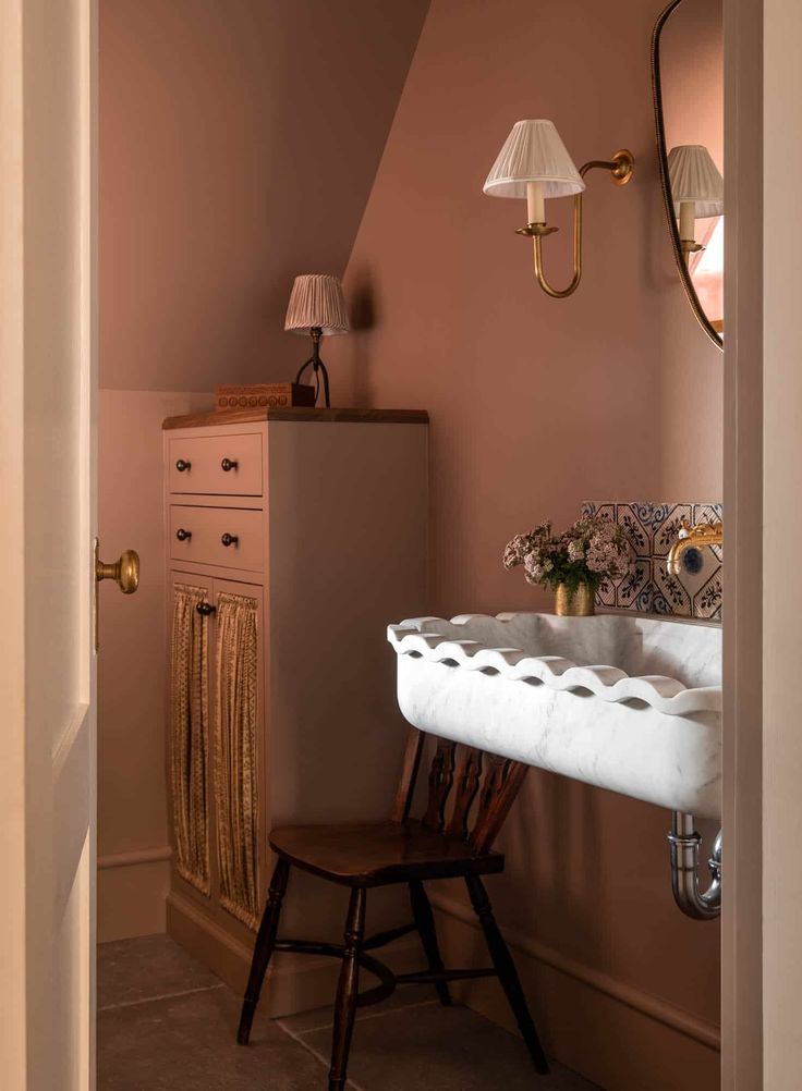 a white sink sitting under a bathroom mirror next to a wooden chair in a room