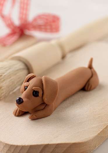 a dog figurine laying on top of a piece of wood next to a paintbrush