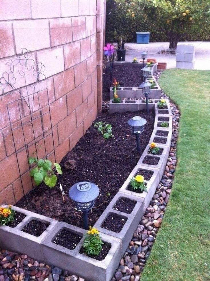 an outdoor garden with various plants and rocks in the ground next to a brick wall