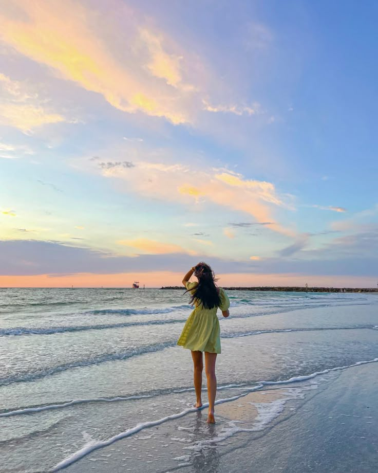 a woman standing on top of a sandy beach next to the ocean at sunset or dawn