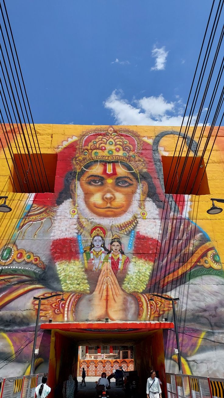 a large mural on the side of a building with people walking underneath it and some wires above